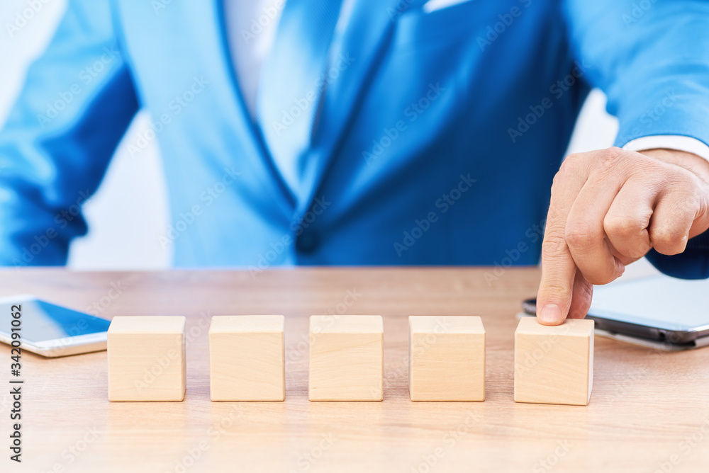 Five wooden cubes lie in a row on the businessman's desk. The man pushes the last cube forward on the table. There is free space on the blocks for letters, numbers, symbols, or inscriptions. Five wooden cubes lie in a row on the businessman's desk. The man pushes the last cube forward on the table. There is free space on the blocks for letters, numbers, symbols, or inscriptions.