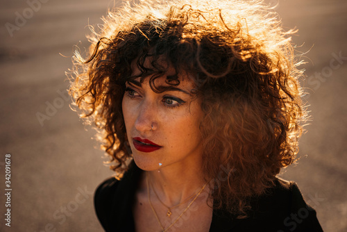 From above of young curly haired woman in trendy outfit on asphalt road on sunny day photo