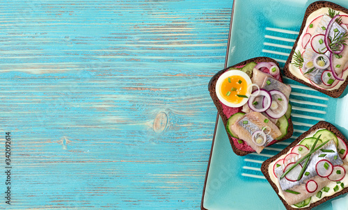 Smorrebrod traditional Danish sandwiches herring, radish, mayonnaise. Open sandwich with rye bread, herring on blue wooden background, top view. Tasty fish smorrebrod. Flat lay
