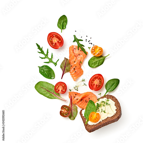 Open sandwich salmon, cherry tomato, spinach, soft cheese flying. Homemade sandwich with rye bread isolated on white background. Levitation fly salmon smorrebrod creative cook concept