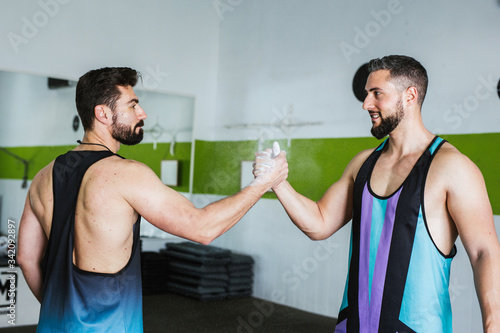 Side view of muscular competitive male bodybuilders with powdered with talcum palms greeting  each other while standing in modern gym photo