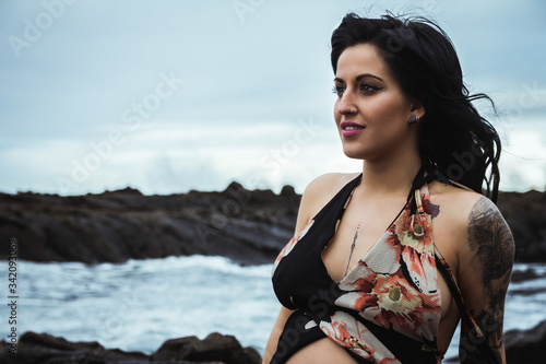 Sensual pregnant woman looking away wearing long waving lingerie robe sitting with bare belly on rocky coast in gloomy day photo