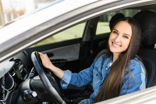 A young girl driving a car. She is in casual jeans jacket looks at camera and smiles © Vadim Pastuh