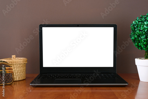 Work space - open laptop with mockup on screen. Wooden containers and green plant in pot. Background of brown wall.