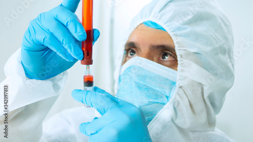 Close up view of latin doctor in bioprotective suit, mask and blue gloves taking a sample from a test tube with a syringe on white background photo