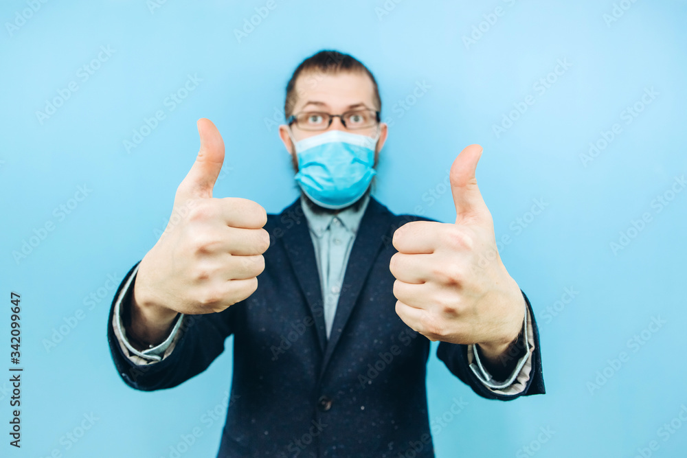 a successful muschin in a suit, glasses and a medical mask on a blue background. Businessman. A private entrepreneur affected by the coronavirus epidemic. Pandemic covid 2019. a successful muschin in a suit, glasses and a medical mask on a blue background. Businessman. A private entrepreneur affected by the coronavirus epidemic. Pandemic covid 2019.
