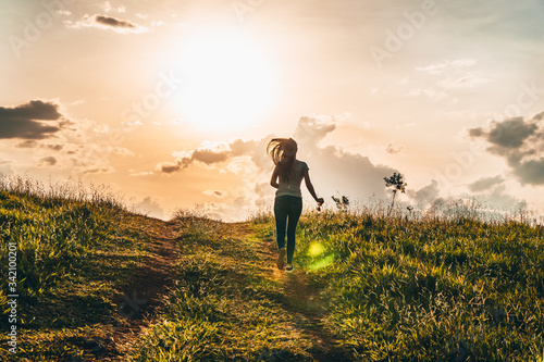 A young girl running on a mountain at sunset. Happy