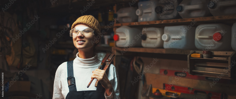 Portrait of smiling young builder girl standing in old workshop room, wearing construction glasses. Portrait of smiling young builder girl standing in old workshop room, wearing construction glasses.