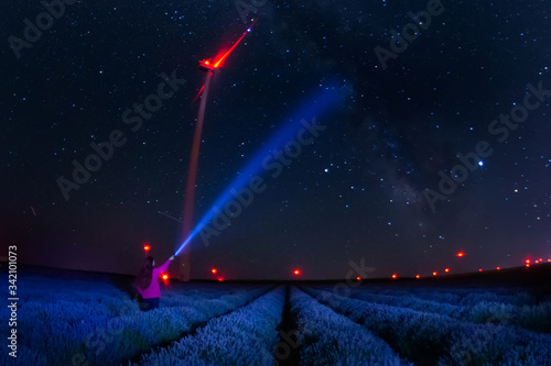 Beautiful landscape of a starry night with milky way and blue sky over a field of lavender and red lights of wind turbines, Gorun, Bulgaria