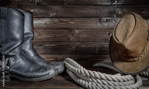 cowboy hat, boots and rope on wooden background