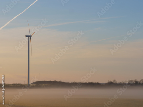 Wind turbines generating renewable energy  morning beautiful sunrise light with drifting fog and amazing clouds background.