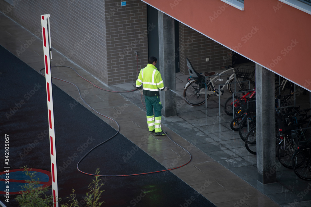 Fototapeta premium Janitor washes the yard with water from a hose.
