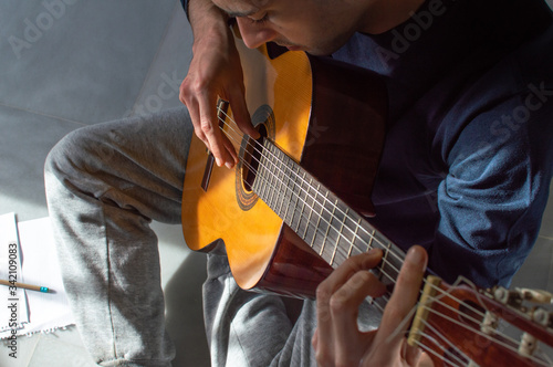 Top view of a young man playing guitar and composing music at home. Casual man sitting on the floor learning guitar.