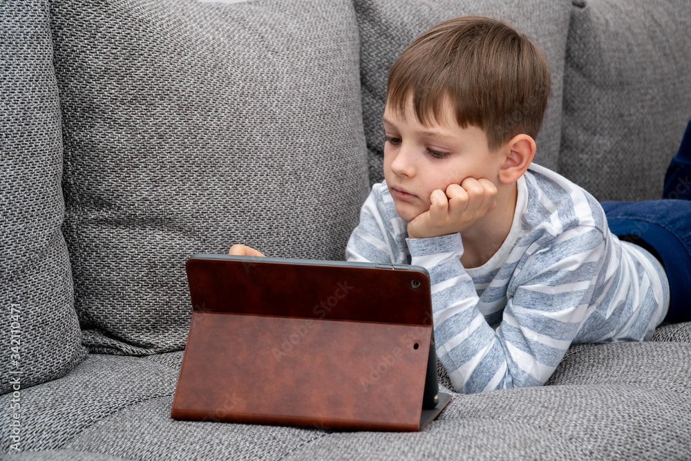 Distance learning online education. School kid in self isolation using tablet for homework,Bored Child sad face lying head down looking out deep in thought, Boy stay at home during covid-19 lock down.