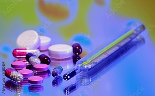  Pills with a thermometer on a colored mirror background