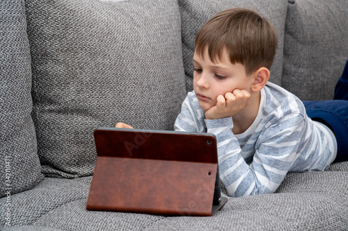 Obraz na płótnie Distance learning online education. School kid in self isolation using tablet for homework,Bored Child sad face lying head down looking out deep in thought, Boy stay at home during covid-19 lock down. w salonie