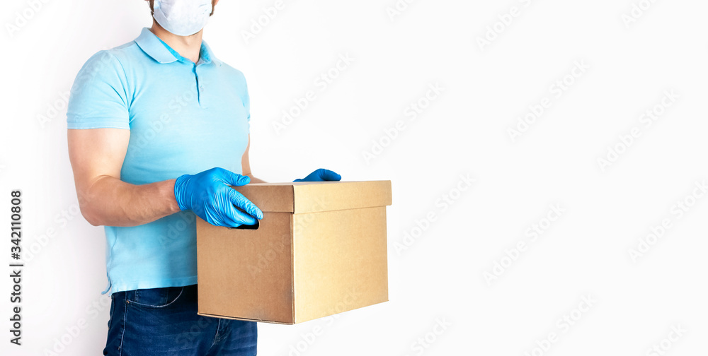 Concept of delivery of goods during quarantine 2019-ncov. Young man with beard in medical mask and blue gloves holds cardboard box in his hands on white background. Contactless delivery virus protect Concept of delivery of goods during quarantine 2019-ncov. Young man with beard in medical mask and blue gloves holds cardboard box in his hands on white background. Contactless delivery virus protect