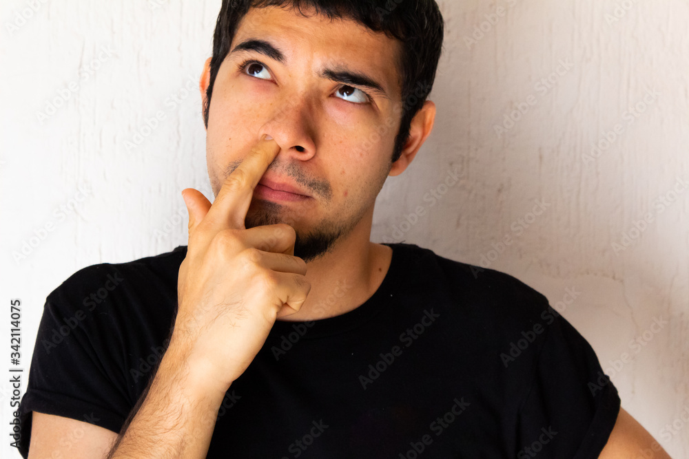 Young short-haired Hispanic man with black clothes, in a thoughtful pose and scratching his nose on a white background Young short-haired Hispanic man with black clothes, in a thoughtful pose and scratching his nose on a white background