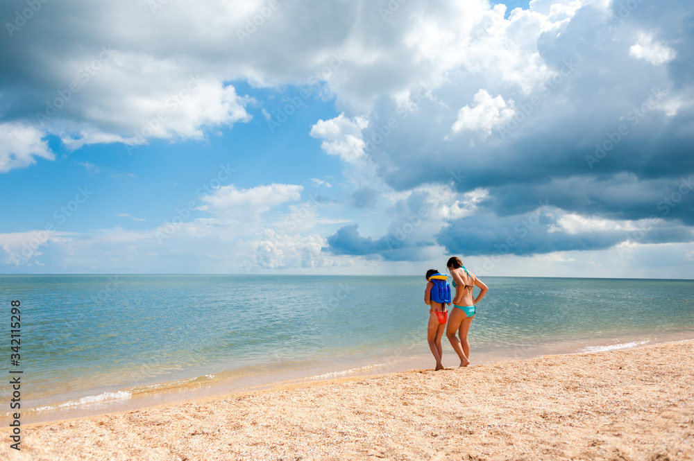 two happy Caucasian girls in swimsuits on a sandy beach by the sea in Sunny weather two happy Caucasian girls in swimsuits on a sandy beach by the sea in Sunny weather