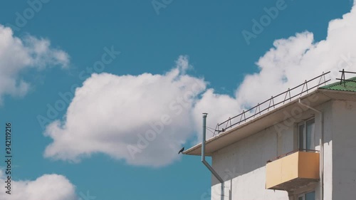 A crow sits on the corner of the roof of the house and flies away