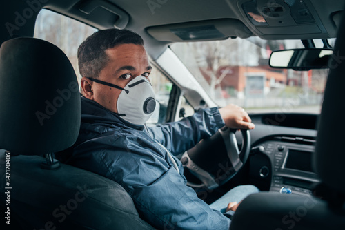 young hispanic taxi driver wearing a protective mask and talks to a client.
