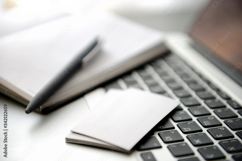 A business card and a paper notebook with a pen on a laptop keyboard. Shallow depth of field. A business card and a paper notebook with a pen on a laptop keyboard. Shallow depth of field.