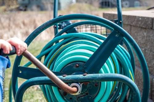 Selective focus on front bar on a wound garden hose storage cart with small child spinning lever