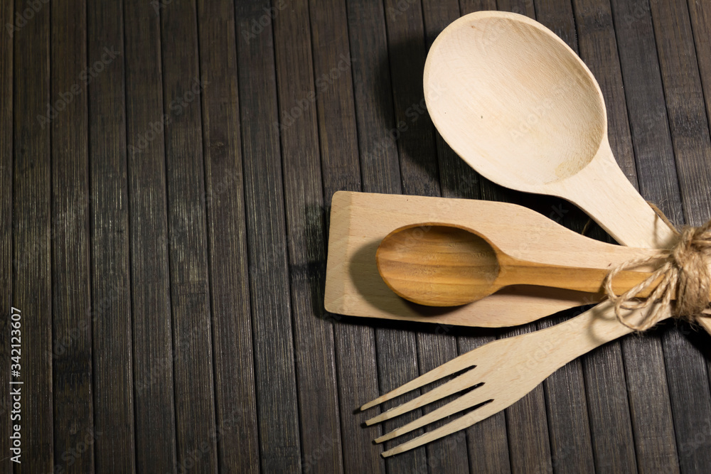 On a wooden dark background are wooden cutlery - small and large spoons, a fork, a spatula, tied with a hemp rope. On a wooden dark background are wooden cutlery - small and large spoons, a fork, a spatula, tied with a hemp rope.
