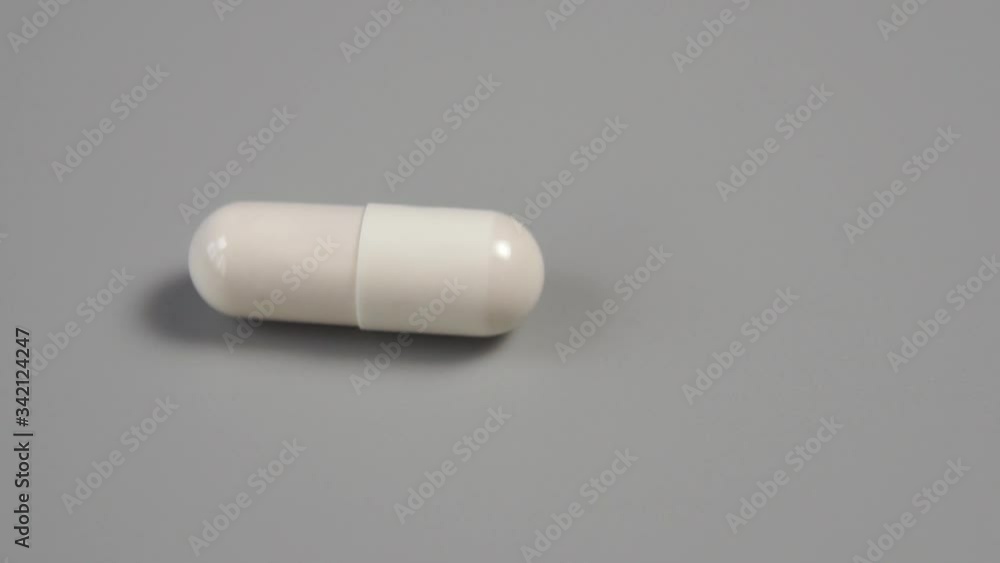 Closeup white capsule spins on a gray plastic surface. Slow motion. Macro shot. Medical concept. Coronavirus vaccine Closeup white capsule spins on a gray plastic surface. Slow motion. Macro shot. Medical concept. Coronavirus vaccine
