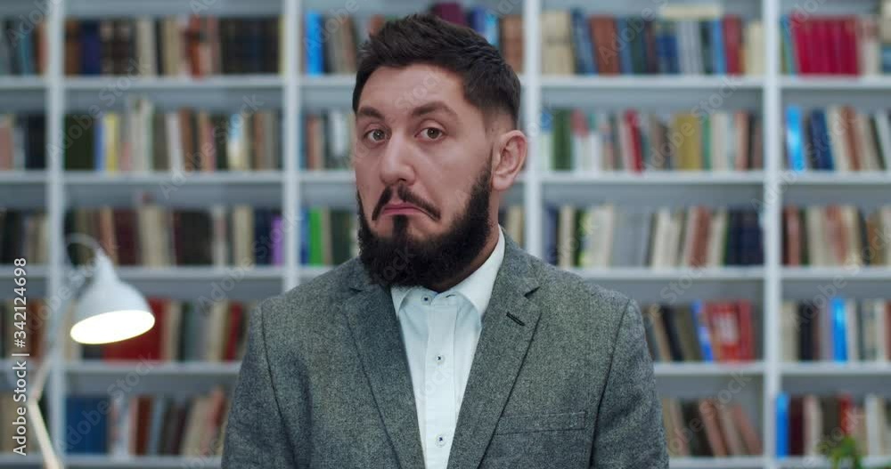 Close up of handsome Caucasian man in jacket with bear standing in front of camera in library with surprised face. Male nodding his head like agreeing and approving something. Study concept. Close up of handsome Caucasian man in jacket with bear standing in front of camera in library with surprised face. Male nodding his head like agreeing and approving something. Study concept.