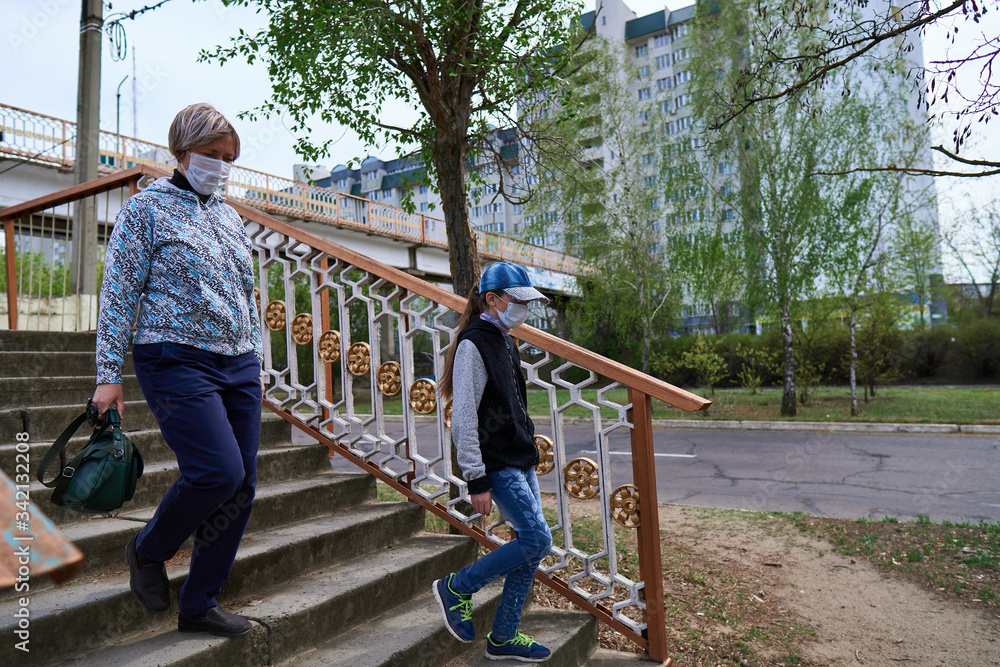 woman and child girl walks down the street during the day, a pedestrian walkway and buildings with apartments, a residential area, a medical mask on their faces protects against viruses and dust woman and child girl walks down the street during the day, a pedestrian walkway and buildings with apartments, a residential area, a medical mask on their faces protects against viruses and dust
