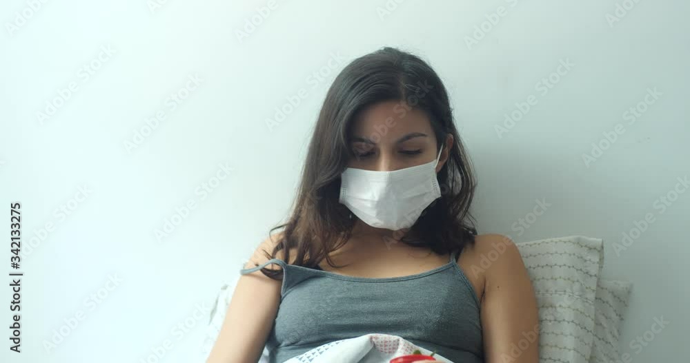 Hispanic Young Brown Hair Female Wears a Disposable Face Mask for Cough, Flu, Virus, Viral Protection. She Stays Home and Waters her Small Plant with a Bottle of Water in Bed Hispanic Young Brown Hair Female Wears a Disposable Face Mask for Cough, Flu, Virus, Viral Protection. She Stays Home and Waters her Small Plant with a Bottle of Water in Bed