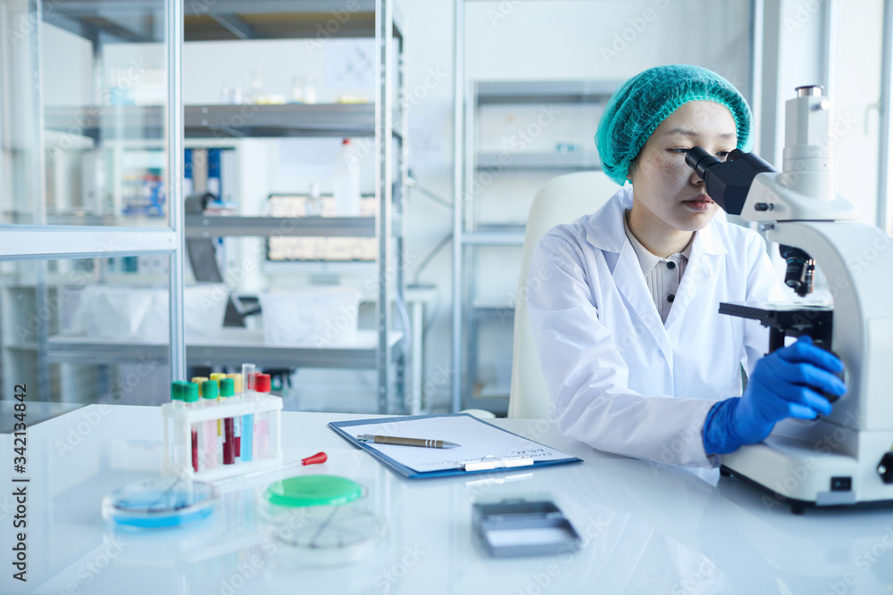Naklejka premium Female doctor looking through the microscope and examining the analysis in the lab