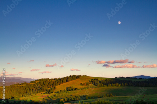 Mountain landscape at sunset. The slopes of the mountains in the evening light. Moon in the evening sky over the mountains