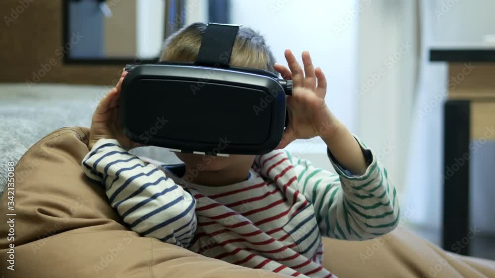 Child wearing virtual reality glasses and watching vr 360 video at home at soft chair bag Child wearing virtual reality glasses and watching vr 360 video at home at soft chair bag
