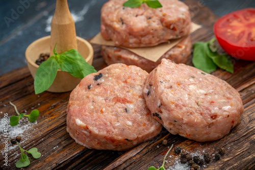 Homemade raw ground beef and Burger Patty with Basil, tomatoes and seasonings on a wooden Board.