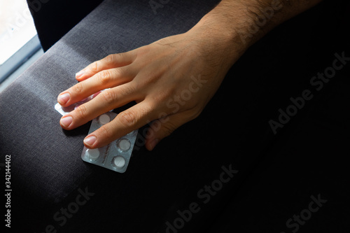 Man sitting on a sofa holding pills with his hand, concept of addictions, disease, medical treatment, pain, health care, medical dependency.