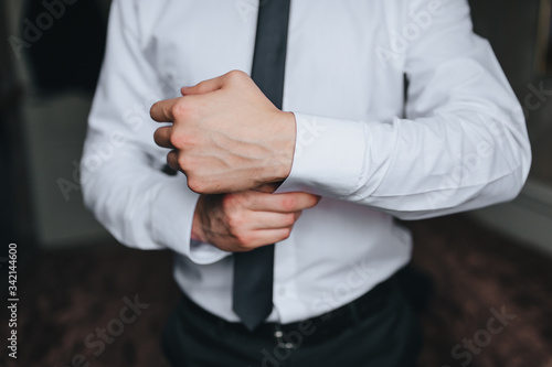 A groom in a white shirt fastens a button on his sleeve. Morning businessman. Preparing for the holiday, work. Photography, concept.
