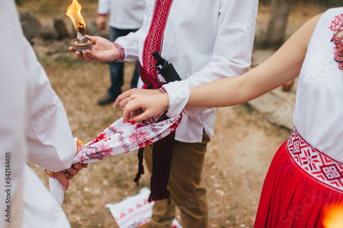 Ataman ties a knot with a towel to the newlyweds at the wedding ceremony of Ukrainian pagans in embroidered shirts holding candles with fire. Photography, concept.