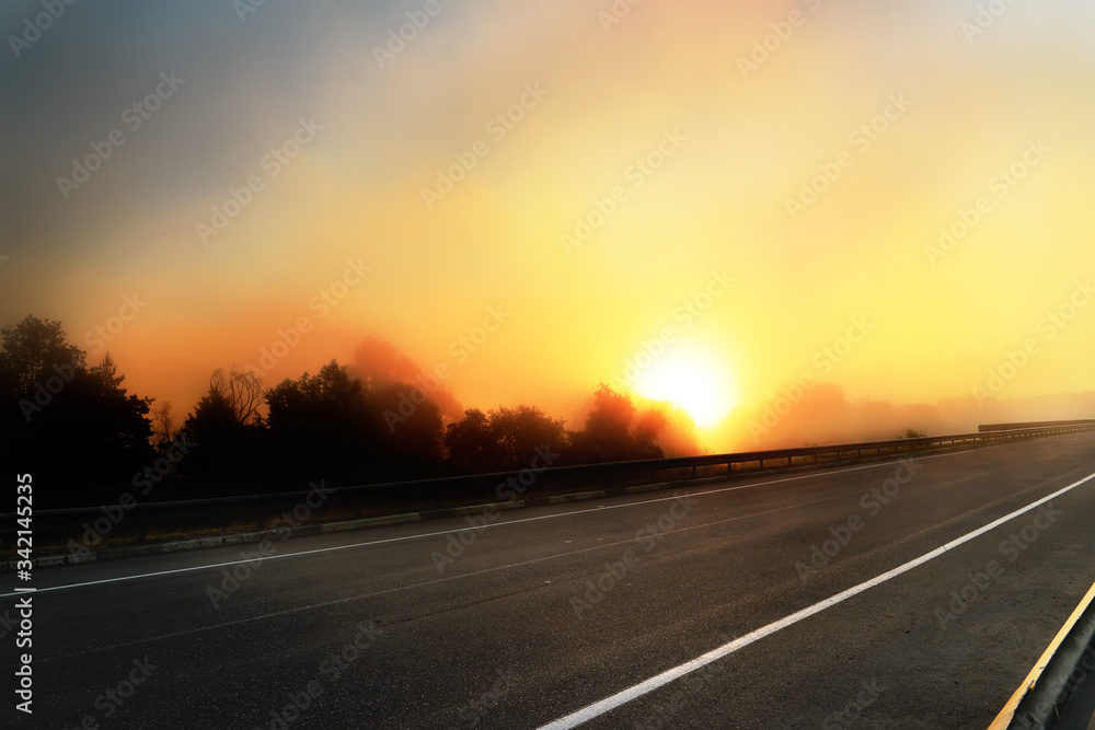 Deserted road and incredible fantastic sunrise. The sun rising due to a foggy cloud backlit by the sun.