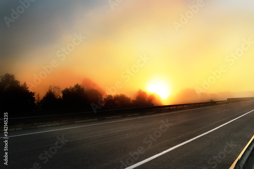 Deserted road and incredible fantastic sunrise. The sun rising due to a foggy cloud backlit by the sun.