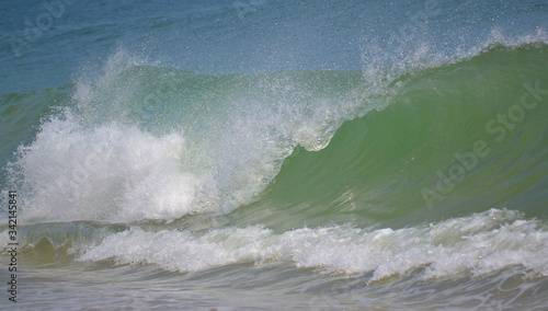 Ocean wave crashing on the shore of water's edge. Blue and green shades of water with white foam.