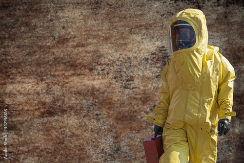 Man with briefcase in yellow protective hazmat suit on brown background.Epidemic virus.  photo