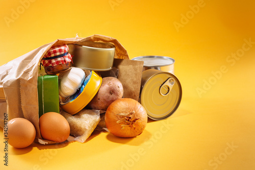 Various groceries inside paper bag on top of yellow background, with available copy space. Stockpiling food concept. photo