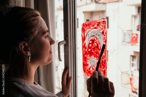 Young woman drawing a Turkish flag on the window at home.  Stay home concept. Celebration in Turkey concept. 