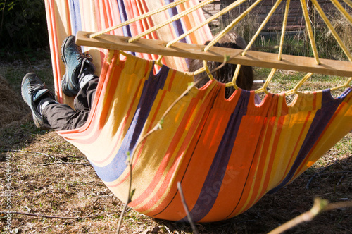  Legs of woman lying in a hammock on the backyard of her country house. Outdoor recreation concept. Country lifestyle. Life in village . pair of shoes 