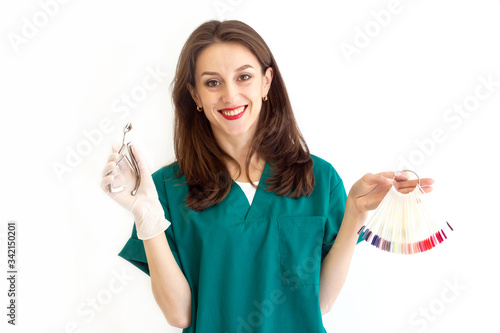 Portrait of a smiling woman, master of nails in a green coat and gloves. The girl holds in her hand a tool for manicure and a palette of gel polishes on a white background. Copy space
