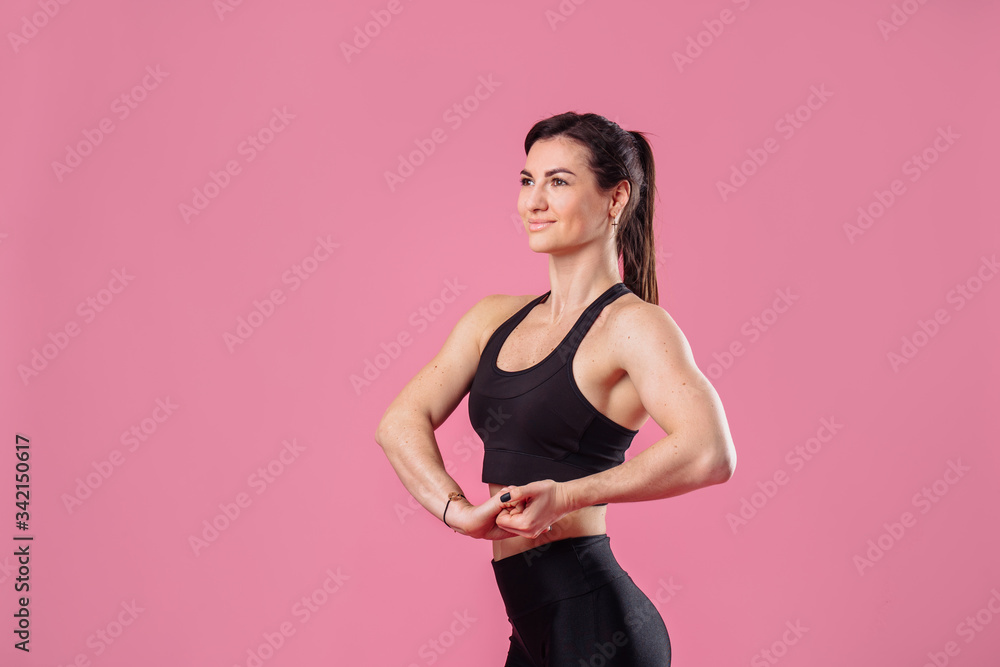 Half lenght portrait of beautiful, pumped up girl in a black tight-fitting top and leggings smiling and showing her big, pumped up muscles in her arms, isolated on pink background in photostudio Half lenght portrait of beautiful, pumped up girl in a black tight-fitting top and leggings smiling and showing her big, pumped up muscles in her arms, isolated on pink background in photostudio