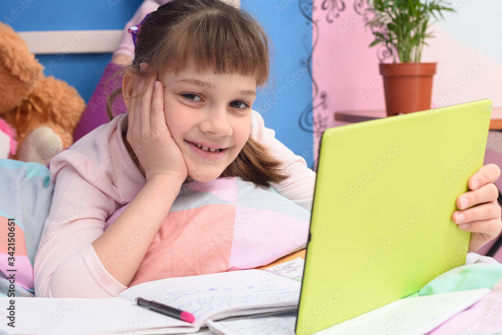 Happy girl lying at home in bed and watching school video lessons Happy girl lying at home in bed and watching school video lessons