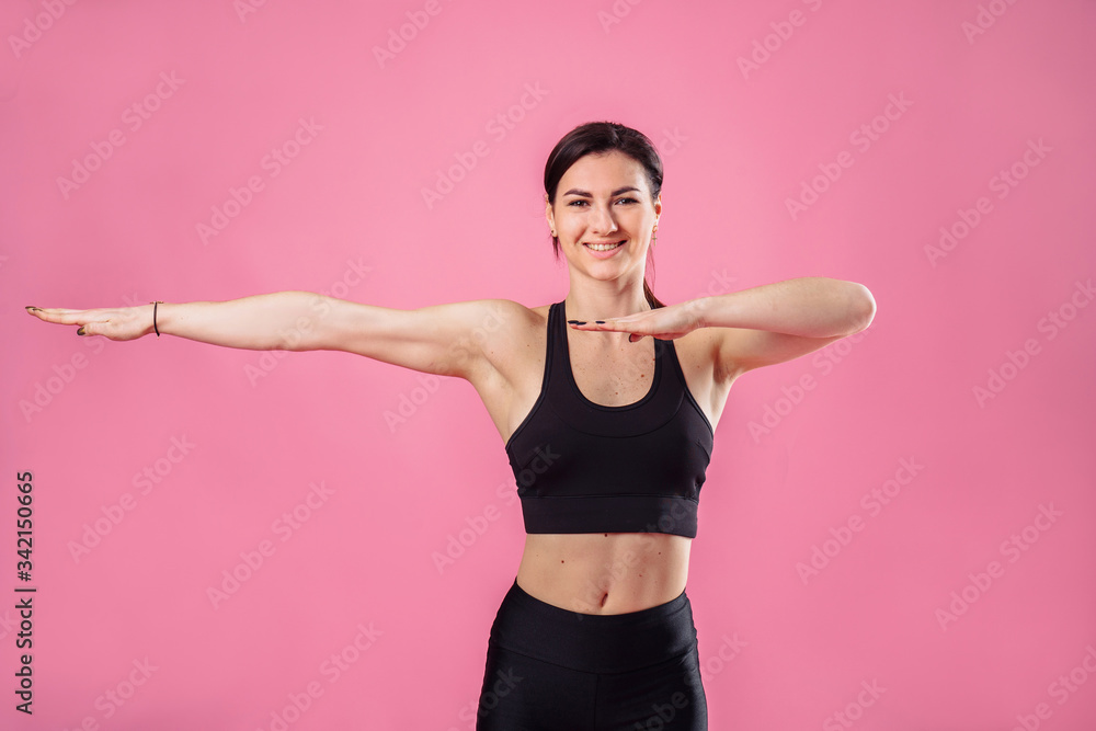 Pumped up sports girl on a pink background in the studio does sports exercises with hands. Smiling and showing her high results by her muscular hands. Fitness for beginners - hands to the side Pumped up sports girl on a pink background in the studio does sports exercises with hands. Smiling and showing her high results by her muscular hands. Fitness for beginners - hands to the side